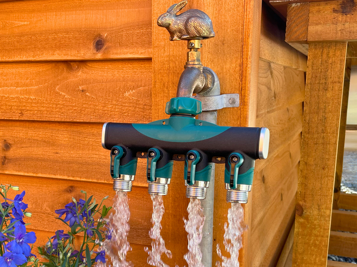 Four streams of water flowing from a green and black hose splitter attached to a rabbit-shaped outdoor faucet