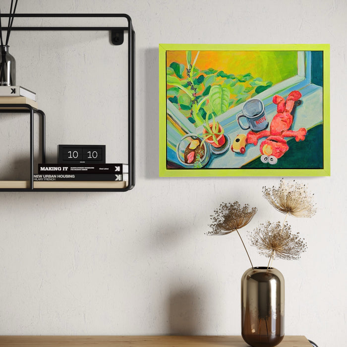 The artwork "And Then She Became the Tree of Heaven" by Mary Younkin depicts a vibrant still life with a bright green-framed acrylic painting on wood panel, featuring lush green leaves, a watering can, and a whimsical red figure with bulbous forms. The composition uses bold, saturated colors and a playful, contemporary style reminiscent of David Hockney’s use of vivid tones and interior scenes.