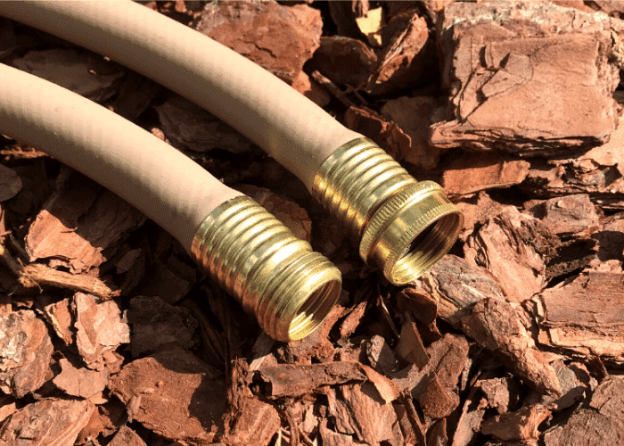 Two beige garden hoses with brass fittings on a bed of wood chips