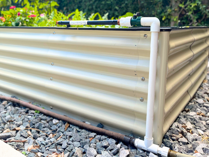 Single Garden Grid Connection Manifold attached to a Garden Grid watering system. Placed in front at the corner of a raised garden bed, with a hose connected at the bottom